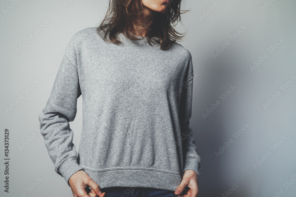 Obraz premium Young hipster girl wearing blank grey cotton sweatshirt with copy space for your design or logo, mock-up of grey template women’s hoodie, white wall in the background