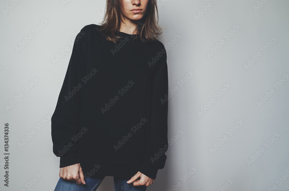 Obraz premium Young pretty girl wearing black template women’s hoodie with copy space for your design or logo, mock-up of black cotton sweatshirt, white wall in the background with area for your content