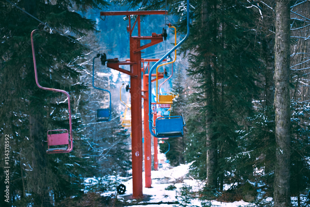 Row line of many pastel colored chairs of retro grunge ski lift, moving through winter pine forest covered in fresh snow in mountains Row line of many pastel colored chairs of retro grunge ski lift, moving through winter pine forest covered in fresh snow in mountains