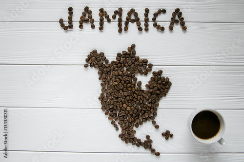 Map of the Jamaica made of roasted coffee beans laying on white wooden textured background with cups of coffee. Space for text.