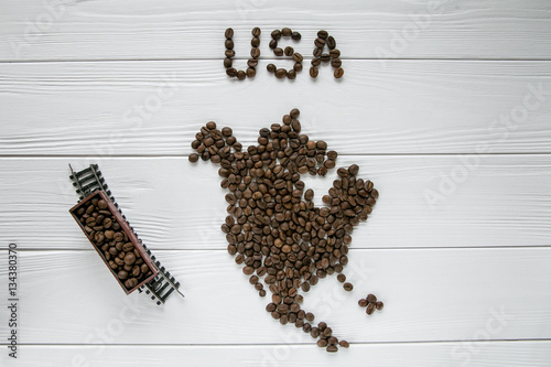 Map of the USA made of roasted coffee beans laying on white wooden textured background with toy train. Space for text