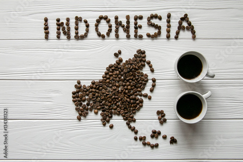 Map of theIndonesia made of roasted coffee beans laying on white wooden textured background with two cups of coffee and coffee maker