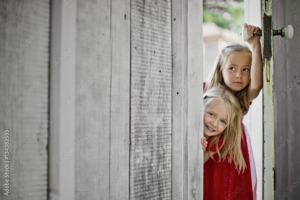 Two young girls peering around a doorframe. Two young girls peering around a doorframe.