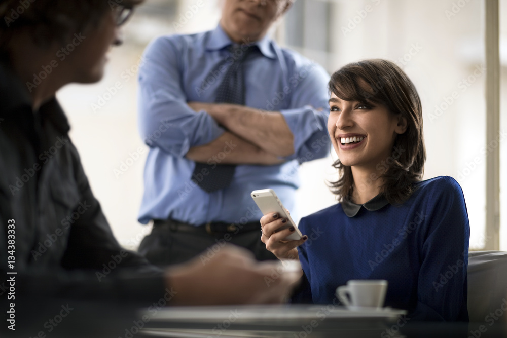 Woman holding a smartphone during meeting with two colleagues Woman holding a smartphone during meeting with two colleagues