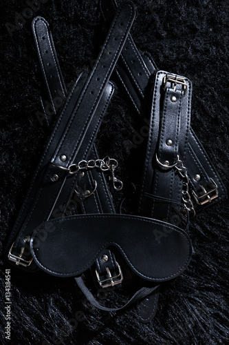 Low key photo of shiny leather cuffs for hands and legs and blinfold for erotic games