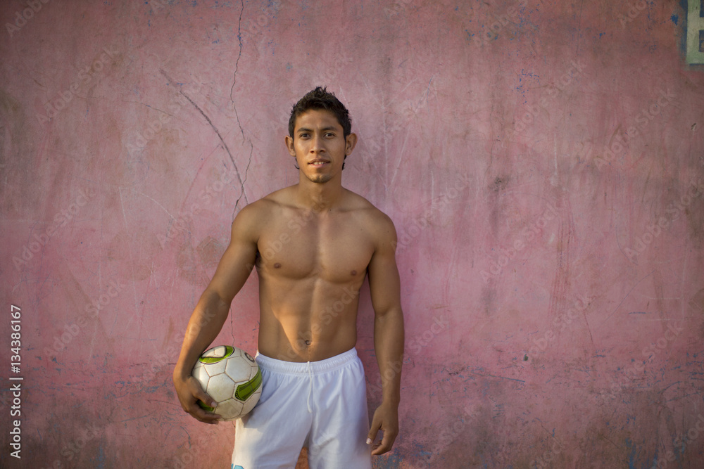 Portrait of a shirtless young man holding a soccer ball while standing ...