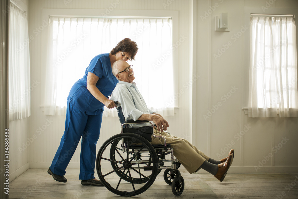 Laughing senior man being pushed in his wheelchair by a female nurse. Laughing senior man being pushed in his wheelchair by a female nurse.