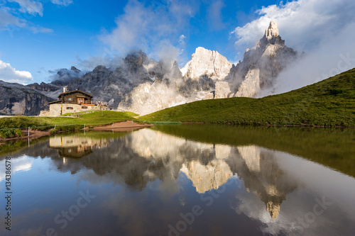 The Pale di San Martino peaks (Italian Dolomites) reflected in the water, with an alpine chalet on background. photo