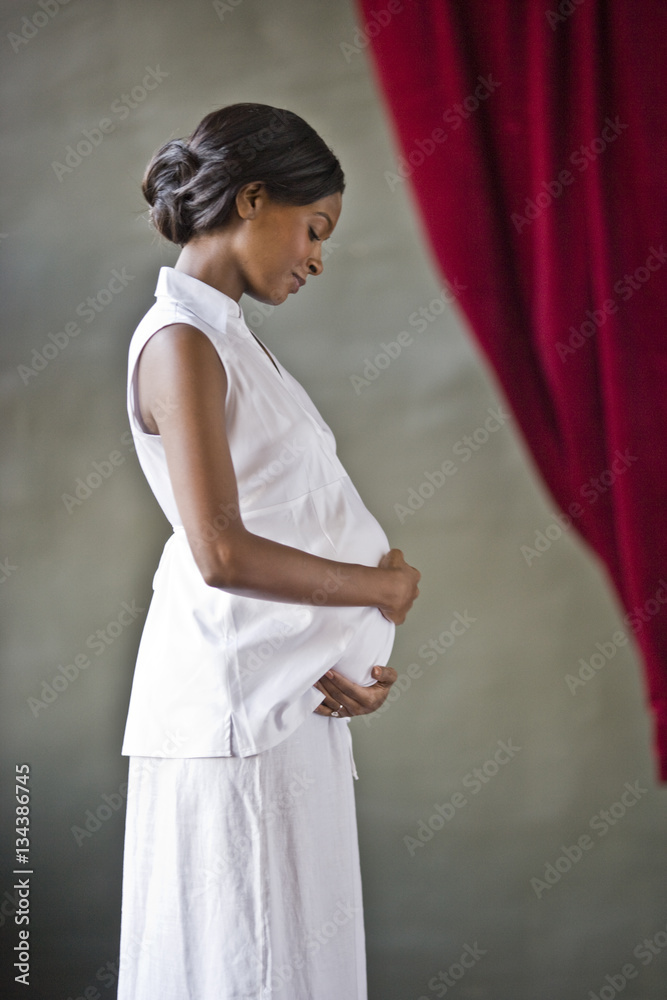 Pregnant mid-adult woman standing with her hand on her belly. Pregnant mid-adult woman standing with her hand on her belly.