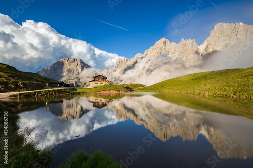 Fototapeta Naklejka Na Ścianę i Meble -  The Pale di San Martino peaks (Italian Dolomites) reflected in the water, with an alpine chalet on background.