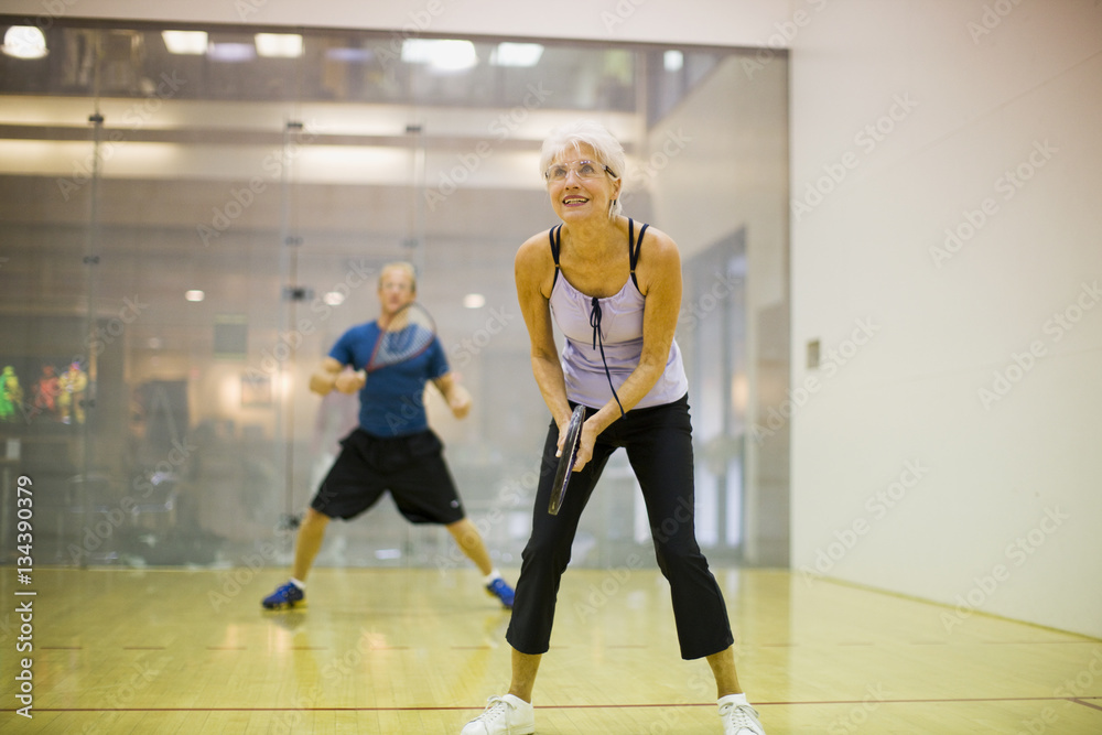 Senior woman playing squash with a mid-adult man. Senior woman playing squash with a mid-adult man.