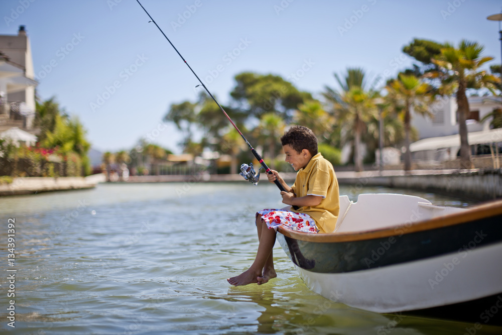 Happy young boy fishing from a small boat in a tropical river. Happy young boy fishing from a small boat in a tropical river.