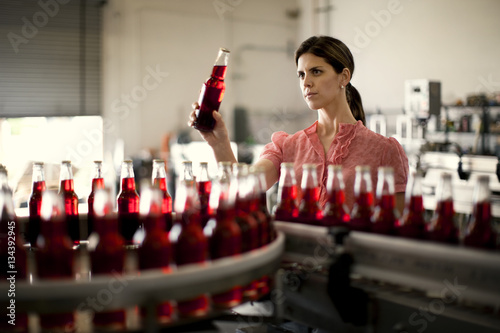 Mid adult woman examining a bottle from a production line.