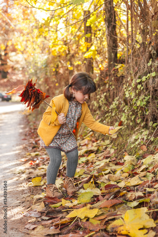 Full shot girl carrying a bouquet of leaves. Autumn background