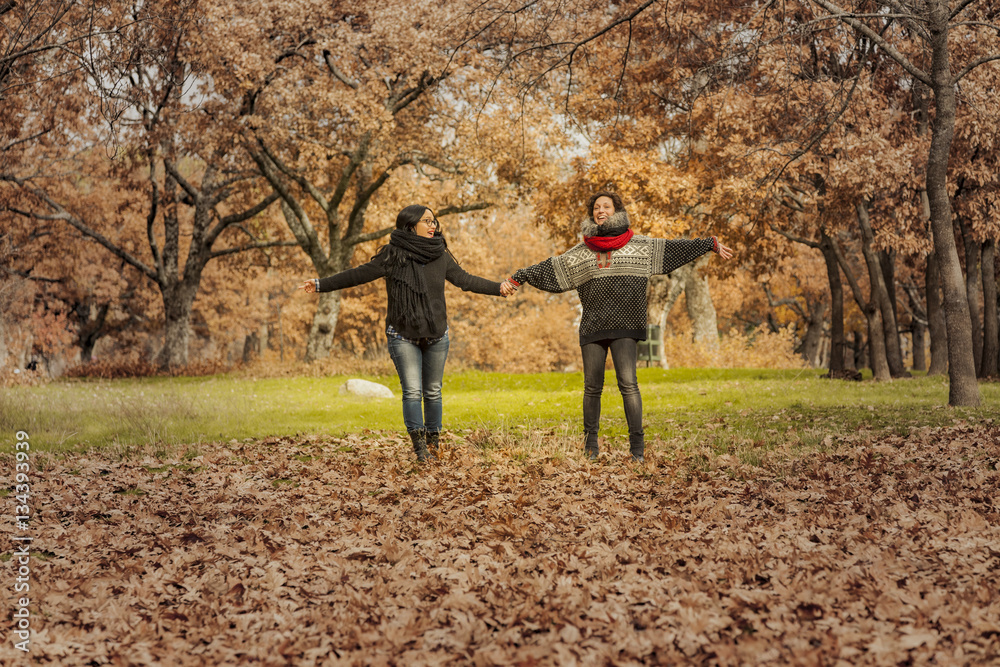 Young women running in the park over a field full of leaves. Aut