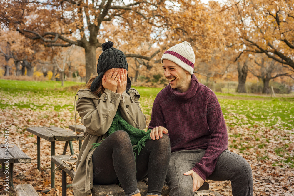 Lovely young couple joking, sit in a bench. Autumn background