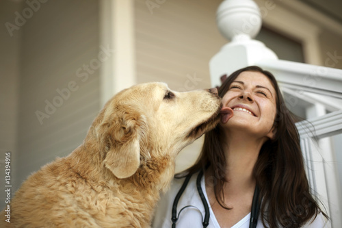 Young female nurse playing with a dog on the verandah of someone's home.