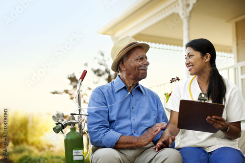 Young female nurse sitting in the garden of an elderly patient with an oxygen tank. photo