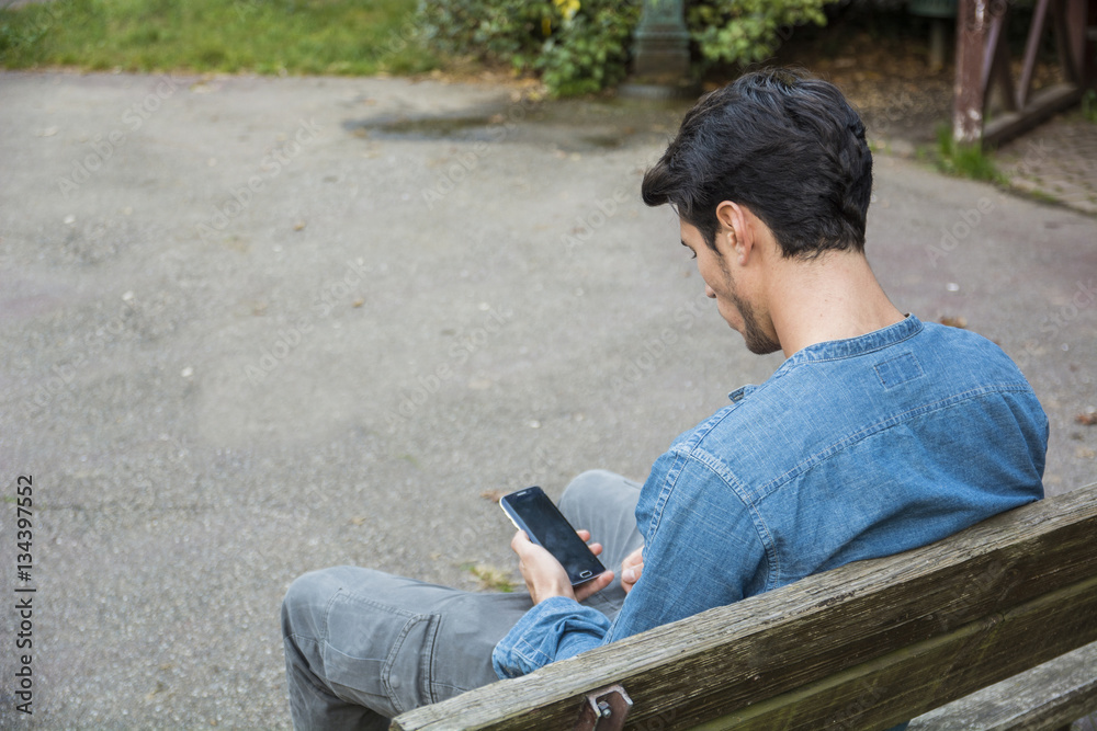 Obraz premium Trendy handsome young man using cell phone sitting on bench