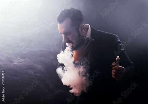 Man coughing out vaponizer holding a vape mod in his hand. photo