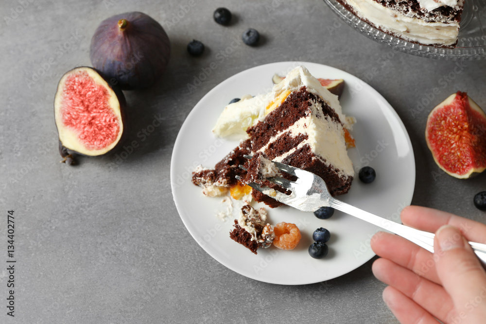Female hand taking piece of delicious creamy cake with figs and berries on grey textured background Female hand taking piece of delicious creamy cake with figs and berries on grey textured background