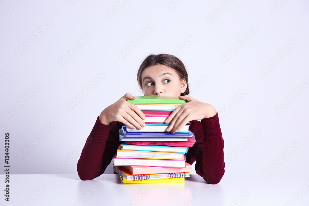Teenage girl with pile of books sitting at table on white background Teenage girl with pile of books sitting at table on white background