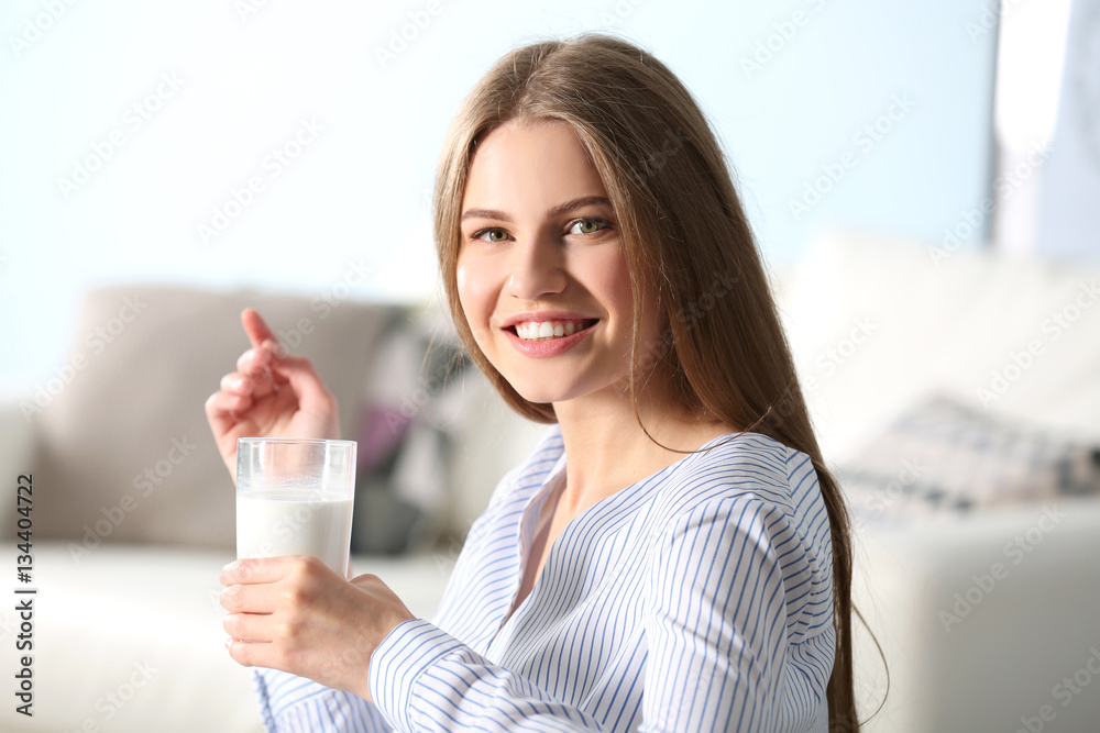 Beautiful young woman with glass of milk at home