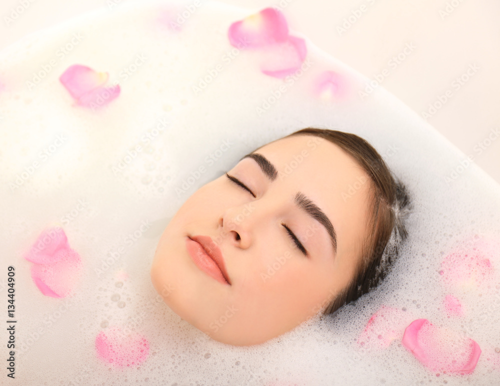 Young attractive woman relaxing in bath with foam and petals, closeup