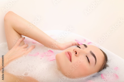 Young attractive woman relaxing in bath with foam and petals  closeup
