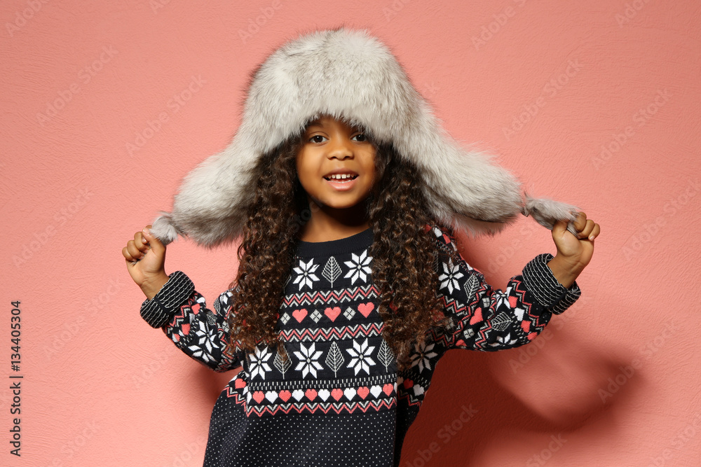 Cute little African American girl in fur hat against pink wall. Fashion concept Cute little African American girl in fur hat against pink wall. Fashion concept