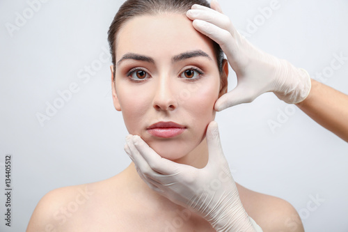 Plastic surgeon examining female face prior to operation, on light background
