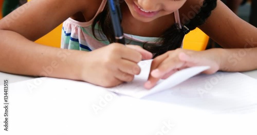 Schoolgirl writing on chit in classroom at school 4k photo