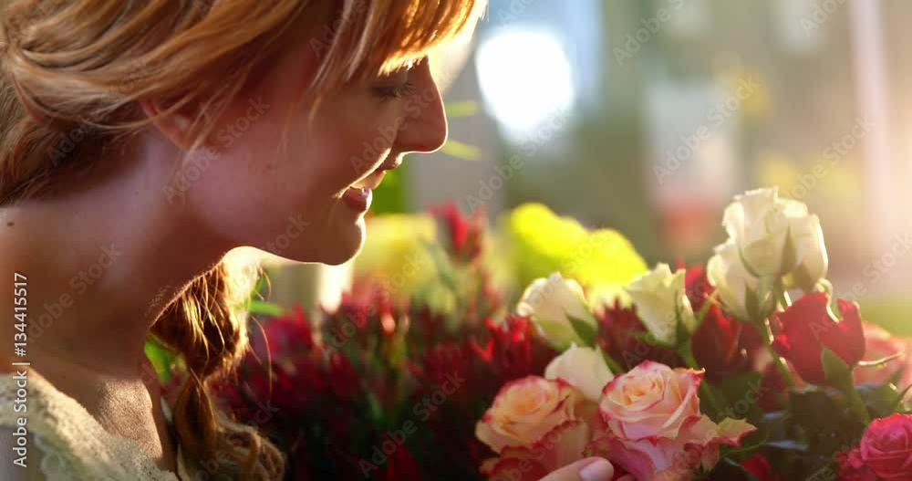 Beautiful female florist smelling pink rose in flower shop