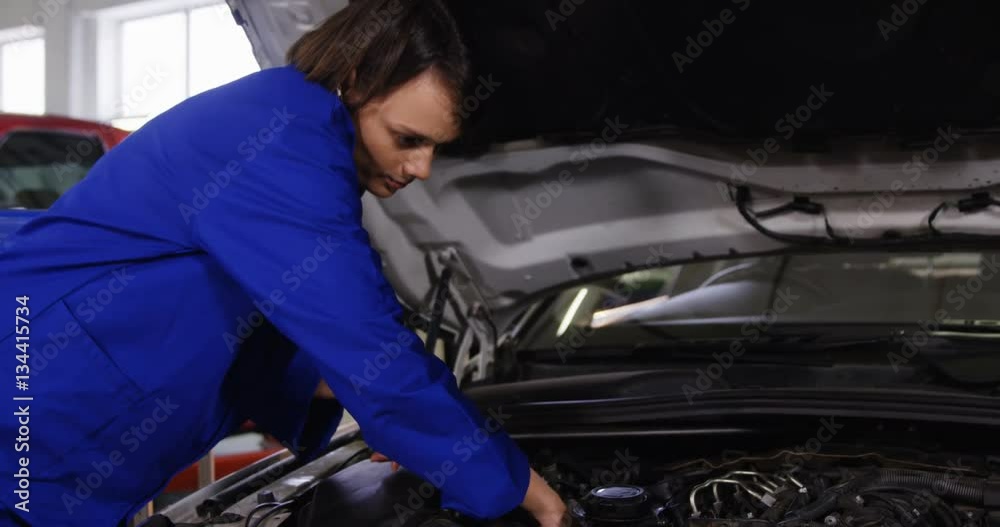 Female mechanic talking on a mobile phone while servicing a car in garage 4k Female mechanic talking on a mobile phone while servicing a car in garage 4k