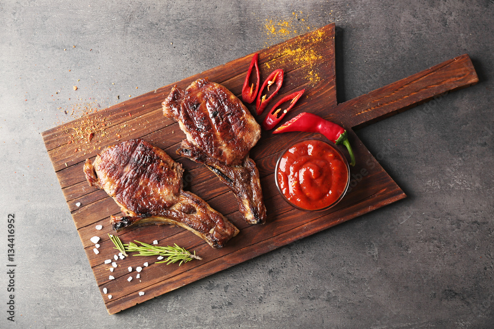 Grilled meat with sauce and chili pepper on cutting board on grey