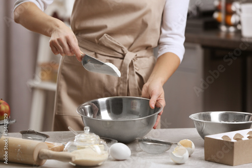 Young woman making dough in kitchen