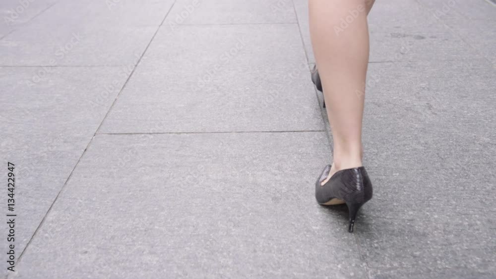 Close-up businesswoman’s feet in heels walking down pavement in city to work Close-up businesswoman’s feet in heels walking down pavement in city to work