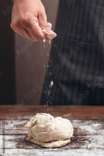Baker sprinkling flour above raw dough. Cook preparing pastry, adding ingredients by recipe. Homemade bakery, cooking process concept