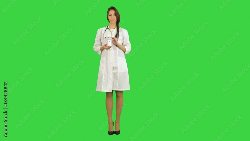 Smiling female doctor looking at camera and recommending jar of pills on a Green Screen, Chroma Key
