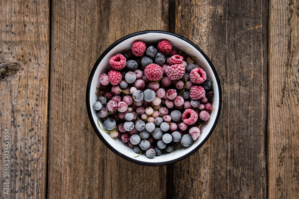 frozen berries, black currant, red currant, raspberry, blueberry in enamel bowl f on wooden table in rustic style, top view. frozen berries, black currant, red currant, raspberry, blueberry in enamel bowl f on wooden table in rustic style, top view.