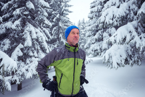 Sporty man with trekking poles stands in the pine forest