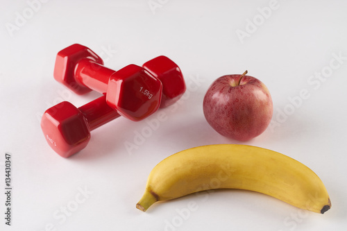 Plastic coated dumbells and fresh fruits: banana, apple on white background