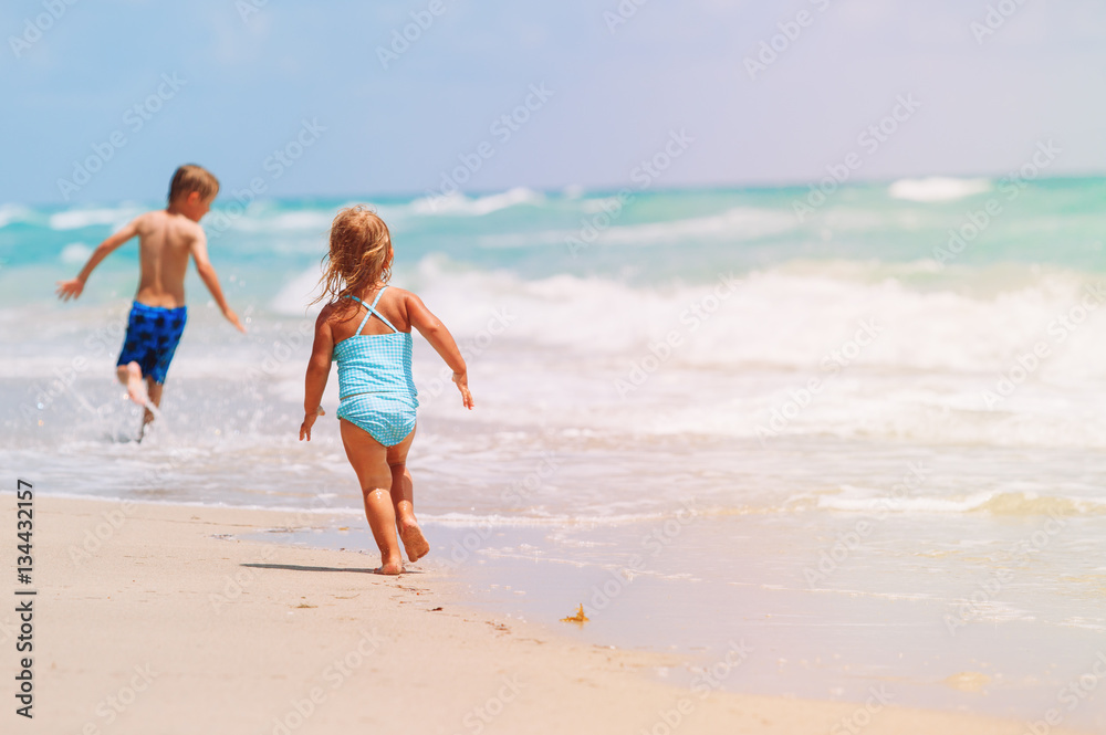 little girl and boy run play with waves on beach