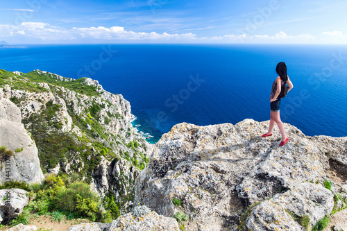 Travel girl stands on the edge of a high cliff above sea. Back view young female. Greece islands landscape. Travel Concept.