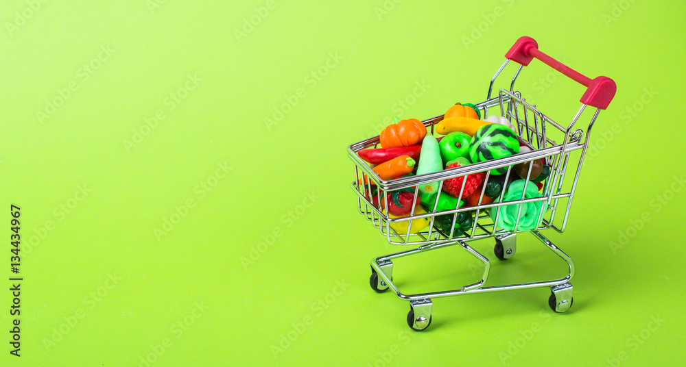 Metal shopping cart with fruits and vegetables on a green background
