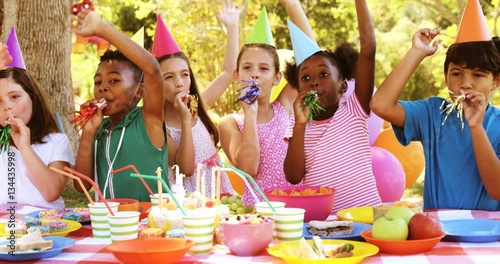 Group of kids blowing party horn while celebrating a birthday in park 4k