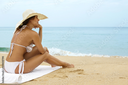 Woman wearing beach hat is sitting beside a sea