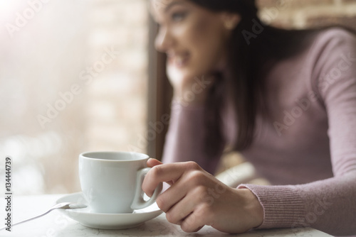 Beautiful young woman drinking coffee sitting by the window in t