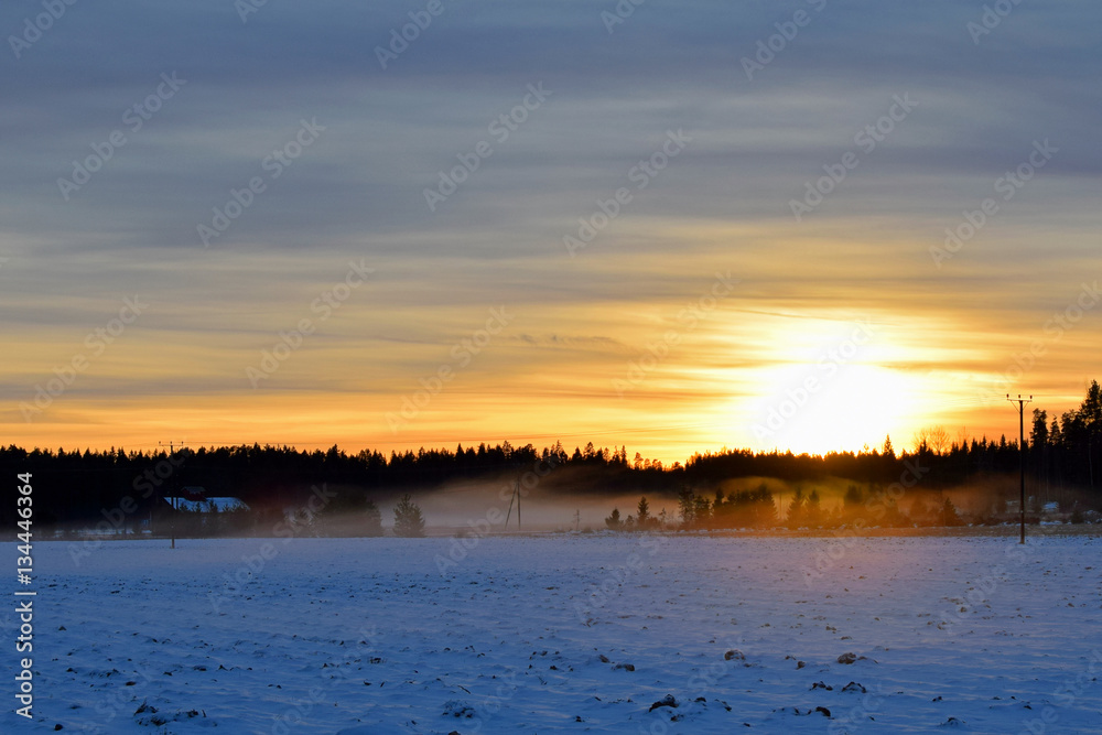 Beautiful sunset on countryside. Snowy field on foreground, mist on background. 