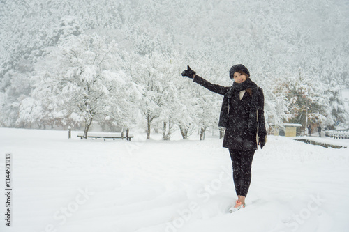Young Asian girl standing in the heavy snow with white background of snow covered tree and mountain 